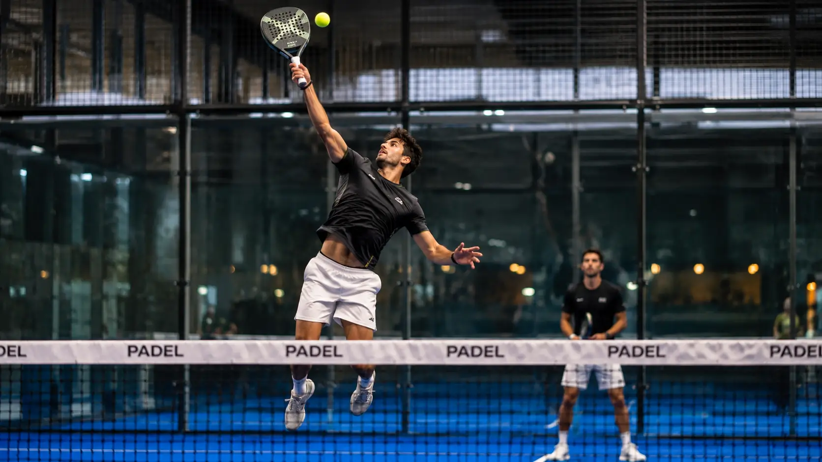 Player executing a flawless Bandeja shot near the net on a panoramic glass padel court at REPPP by Rackonnect