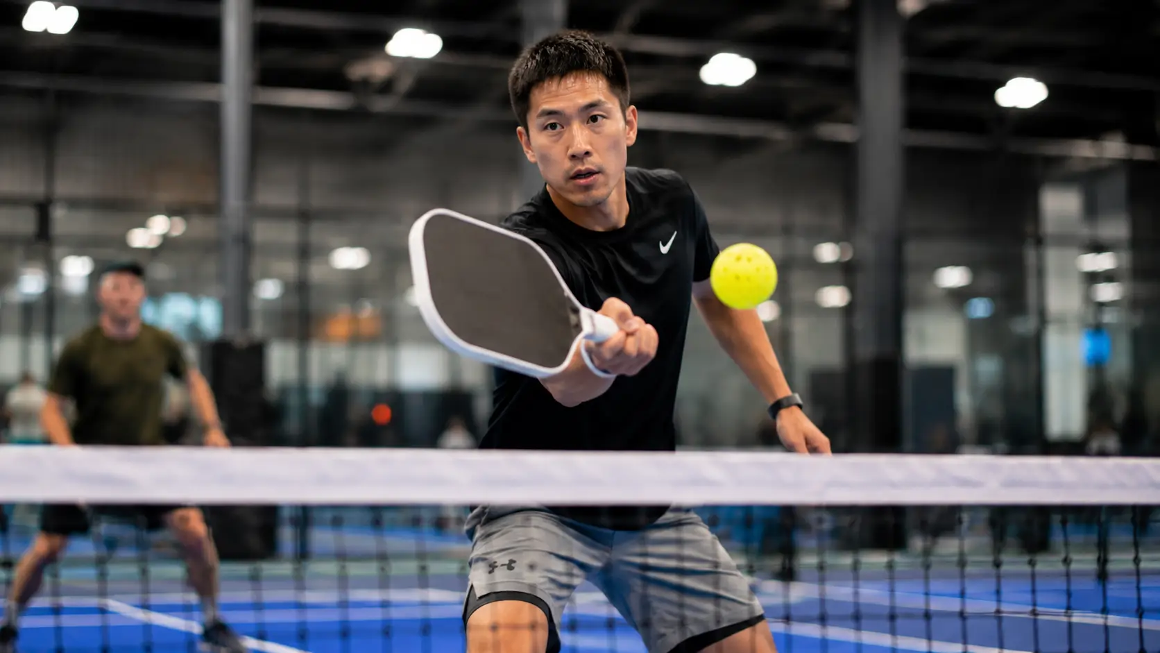 Player hitting a pickleball on a vibrant indoor court showing clear lighting and cushioned synthetic surface traction